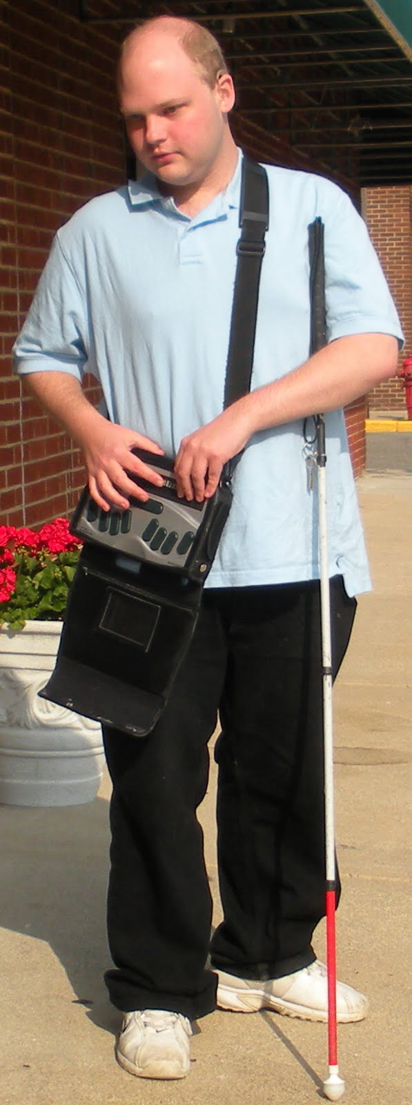 Photo of Scott Davert, standing on the sidewalk with his white cane and assistive technology