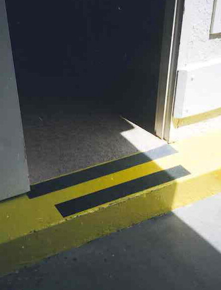 Photo of a step and threshold marked with yellow paint and black marking tape to increase its visibility