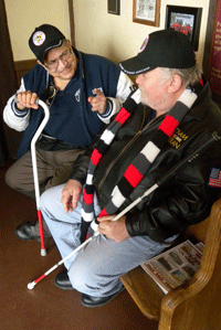 two men, one with mobility cane, the other with a white cane, talking and smiling