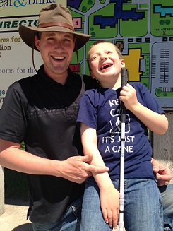 Eddie, holding his white cane, and laughing with his dad