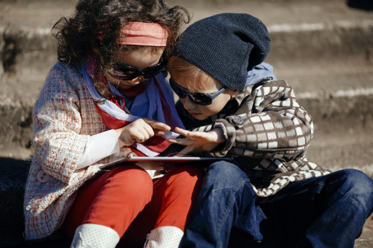 little girl and boy, both wearing sunglasses, playing with an iPad outside